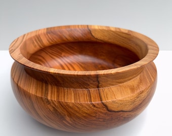 Op de afbeelding: Een ronde houten kom met een opvallend, wervelend nerfpatroon in tinten van warm amber, honing en donkerbruin. De kom heeft een gladde, gepolijste afwerking met een brede, platte rand die naar binnen buigt richting het diepe midden.
