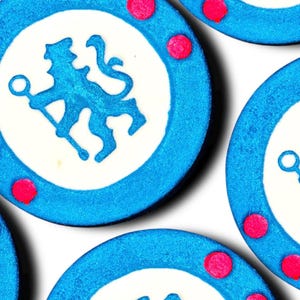 Könnte beinhalten: Nahaufnahme mehrerer blauer und weißer kreisförmiger Objekte mit einem blauen Löwenemblem in der Mitte. Jeder Kreis hat drei rosa Punkte und einen blau glitzernden Rand. Die Objekte sind auf weißem Hintergrund angeordnet.