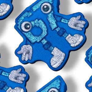 May include: Close-up of several blue robot-shaped objects with silver accents. Each robot has two eye-like circles, arms, and legs. The robots are on a white background.