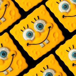 Puede incluir: Patrón repetido de galletas amarillas de forma cuadrada, cada una decorada con una cara sonriente que se asemeja a un popular personaje de dibujos animados. Los ojos son azules y blancos, y la boca tiene dos dientes. Las galletas están dispuestas sobre un fondo negro.