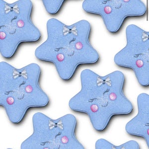 Puede incluir: Una colección de bombas de baño en forma de estrella azul claro. Cada bomba de baño presenta un lazo plateado, ojos cerrados y mejillas rosadas. Las bombas de baño están dispuestas sobre un fondo blanco, creando una estética caprichosa y juguetona.