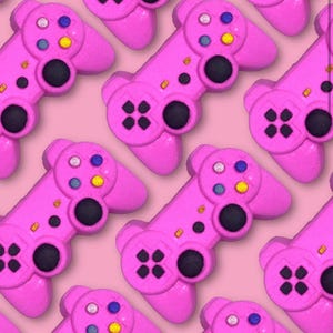 May include: A pattern of pink game controllers with black buttons and colorful accent buttons. The controllers are arranged diagonally on a pink background, creating a playful and repetitive design.