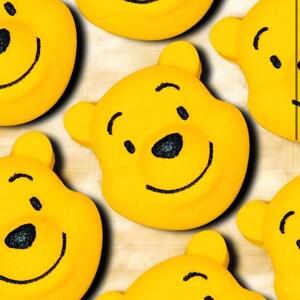 Puede incluir: Primer plano de varias bombas de baño amarillas con forma de oso y rasgos faciales negros. Las bombas de baño tienen una cara sonriente, orejas pequeñas y forma redonda. El fondo es de color claro.