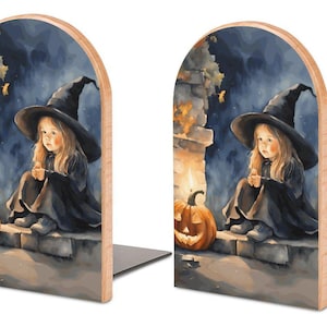May include: Pair of wooden bookends featuring a watercolor illustration of a young witch with a black hat and dress, sitting next to a jack-o'-lantern. The background is a dark, atmospheric scene with a stone wall and a night sky.