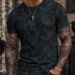 Pode incluir: Uma t-shirt de manga curta com gola redonda, apresentando um padr&atilde;o de floresta em verde escuro e preto com silhuetas subtis de p&aacute;ssaros. A t-shirt &eacute; combinada com cal&ccedil;as de ganga cinzento-escuras com uma corrente prateada na cintura.