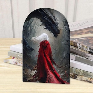 K&ouml;nnte beinhalten: Eine bogenf&ouml;rmige Dekoplatte mit einer Fantasy-Illustration einer Figur mit langem wei&szlig;em Haar und einem leuchtend roten Kapuzenumhang, die in einem dunklen, nebligen Wald einem gro&szlig;en, detaillierten schwarzen Drachen mit scharfen Schuppen gegen&uuml;bersteht.