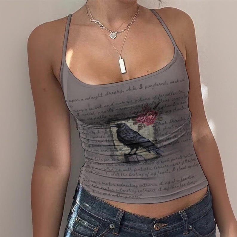 May include: A grey sleeveless vest top featuring a scoop neckline and thin straps. The fabric is printed with dark cursive script text and a central graphic of a black raven perched on a branch with small pink flowers above it.