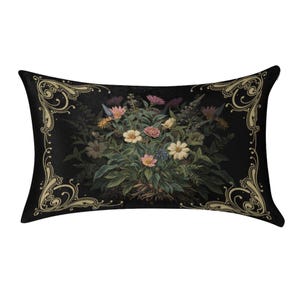 May include: A rectangular throw pillow featuring a black background with a central bouquet of multi-colored flowers including pink, yellow, and white blossoms. The pillow is framed by ornate, light gold scrollwork patterns in each corner.