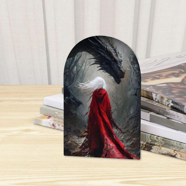 K&ouml;nnte beinhalten: Eine bogenf&ouml;rmige Dekoplatte mit einer Fantasy-Illustration einer Figur mit langem wei&szlig;em Haar und einem leuchtend roten Kapuzenumhang, die in einem dunklen, nebligen Wald einem gro&szlig;en, detaillierten schwarzen Drachen mit scharfen Schuppen gegen&uuml;bersteht.