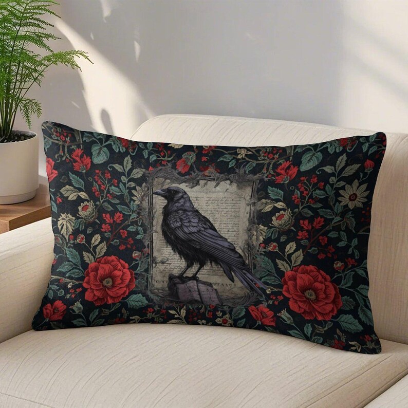 May include: A rectangular throw pillow featuring a black raven perched on a book within a central frame, surrounded by a dark background pattern of red roses, green leaves, and small white flowers on a black fabric surface.