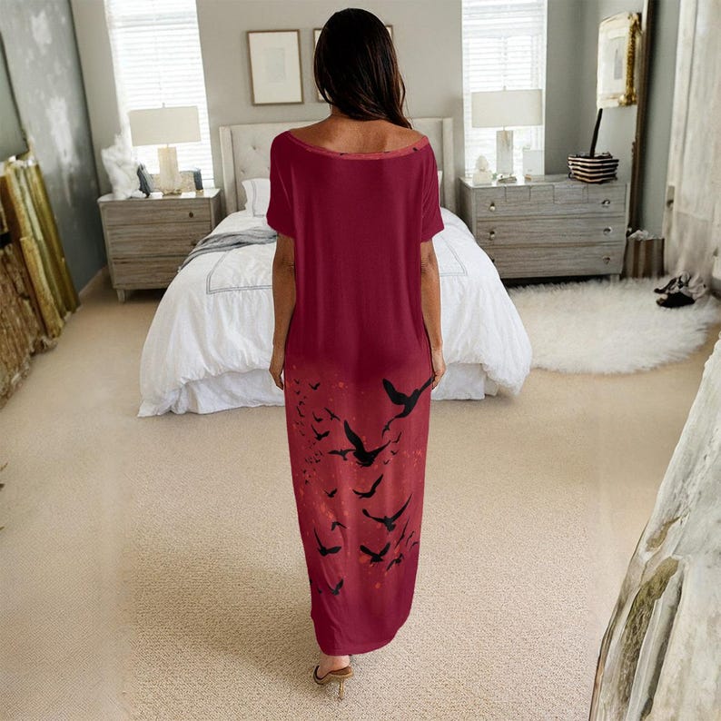 May include: A floor-length, short-sleeved dress in a deep burgundy red color. The garment features a wide, rounded neckline and a loose, flowing silhouette. The lower portion of the dress is decorated with a black graphic print of flying birds.