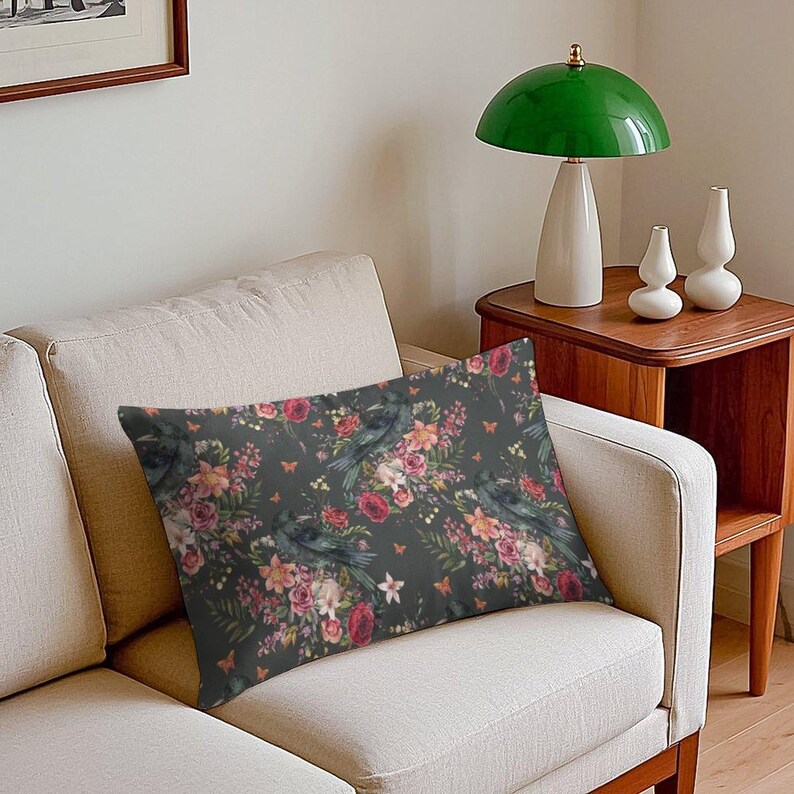 May include: A rectangular throw pillow featuring a dark gray background with a repeating pattern of black crows, vibrant red roses, pink flowers, green fern leaves, and small orange butterflies printed across the fabric surface.