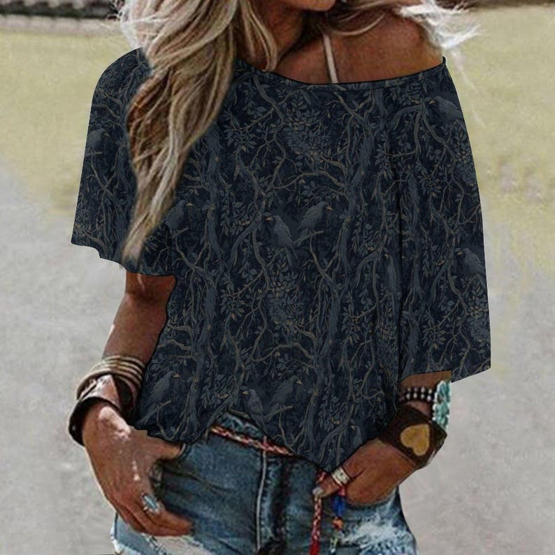 May include: A dark charcoal gray short-sleeved top featuring an intricate, repeating pattern of silhouetted birds perched within dense, tangled tree branches and foliage. The garment has a wide, rounded neckline and a loose, relaxed fit.