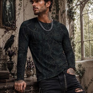 Pode incluir: Uma camisola de manga comprida e gola redonda num tom verde floresta escuro, com um padr&atilde;o tonal intrincado de ramos entrela&ccedil;ados, folhas e p&aacute;ssaros escondidos. A pe&ccedil;a &eacute; combinada com cal&ccedil;as de ganga pretas desgastadas com rasgos nos joelhos.