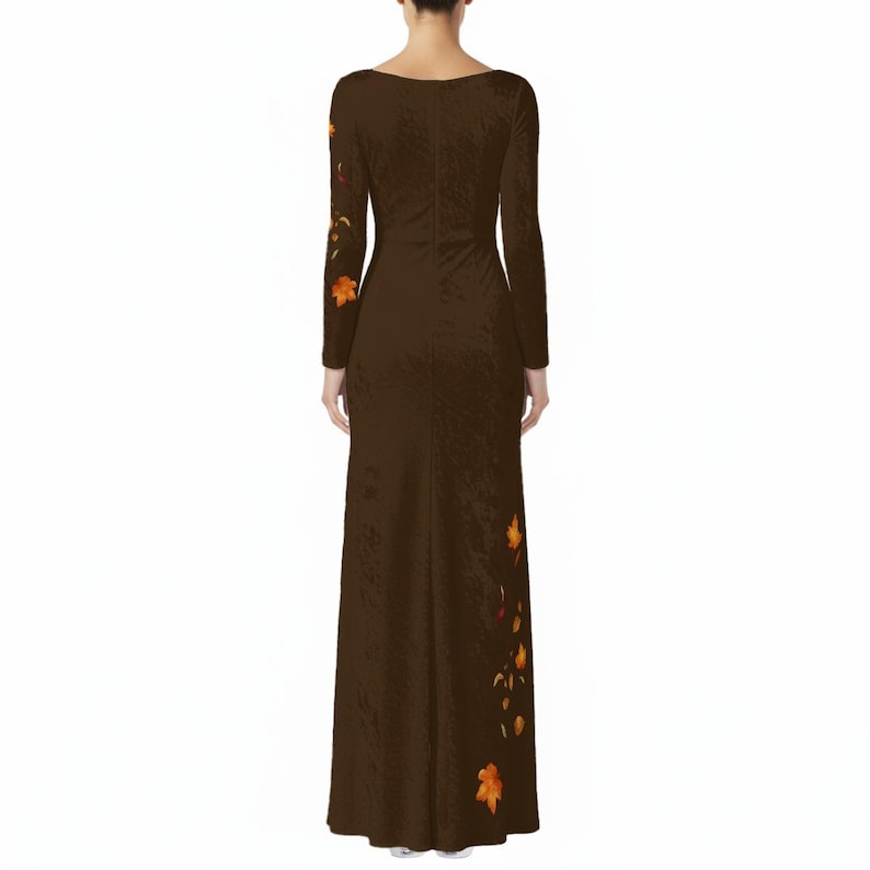 May include: A floor-length, long-sleeved dark brown dress featuring a subtle, textured fabric finish. The garment is adorned with a scattered pattern of vibrant orange and yellow autumn leaves, concentrated along the right sleeve and the lower left side.
