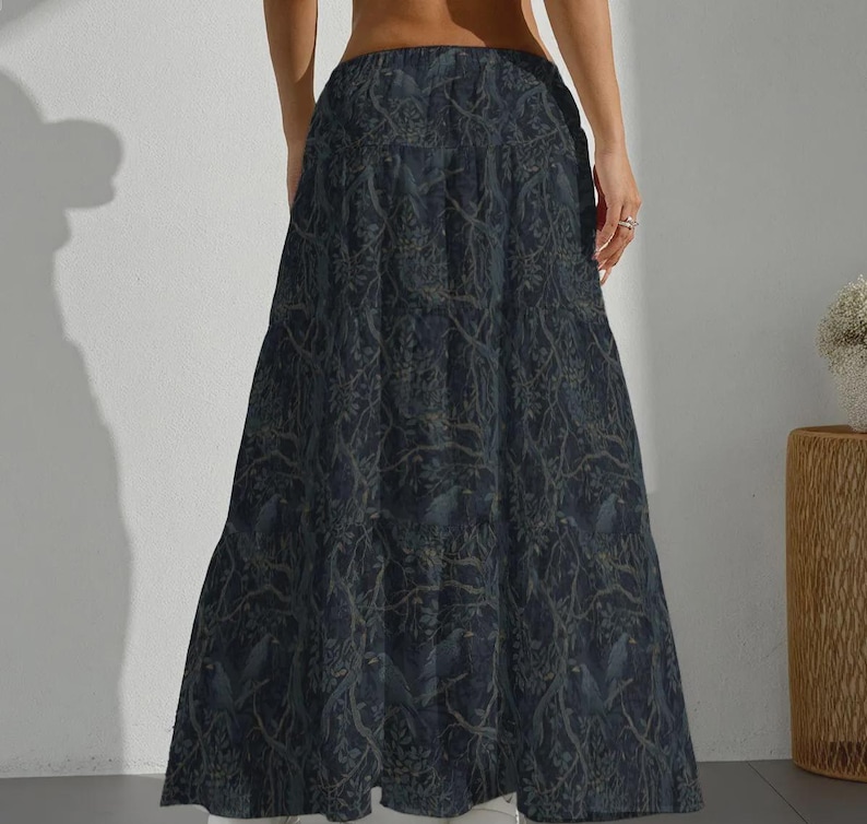 May include: A floor-length, high-waisted maxi skirt in a dark navy blue hue. The fabric features an intricate, repeating pattern of intertwined tree branches and foliage in a muted, lighter blue-grey tone, creating a dense, layered visual effect.