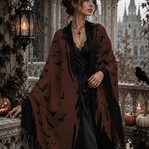 May include: A brown shawl featuring a black bat pattern and black fringe trim. The shawl is worn over a black satin wrap dress with lace detailing at the neckline. The garment is draped over the shoulders, showcasing the contrast between the brown fabric and the black bat silhouettes and the solid black border.