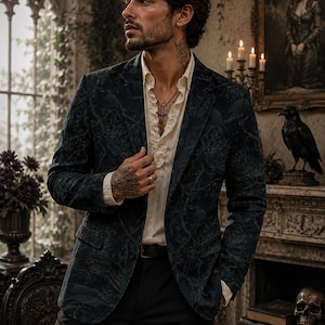 Pode incluir: Um blazer verde-escuro com um padr&atilde;o tonal subtil de aves e motivos bot&acirc;nicos, usado sobre uma camisa cor de creme com carcela de folhos. O blazer apresenta lapelas de entalhe, dois bolsos frontais e um design de abotoamento simples.