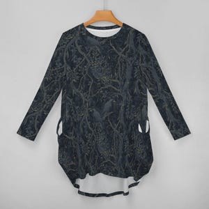 May include: A long-sleeve tunic top featuring a dark, moody forest pattern with black crows perched on tangled tree branches. The garment has a rounded neckline, a high-low hemline, and two side pockets integrated into the dark, leafy print design.