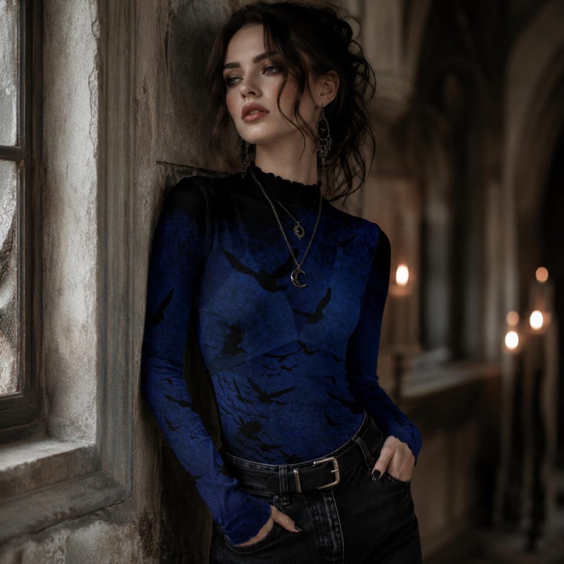 May include: A long-sleeved mock neck top in a deep blue hue featuring a repeating black bird silhouette pattern. The garment is paired with black denim jeans secured by a black leather belt with a silver buckle, and accessorized with a silver necklace.
