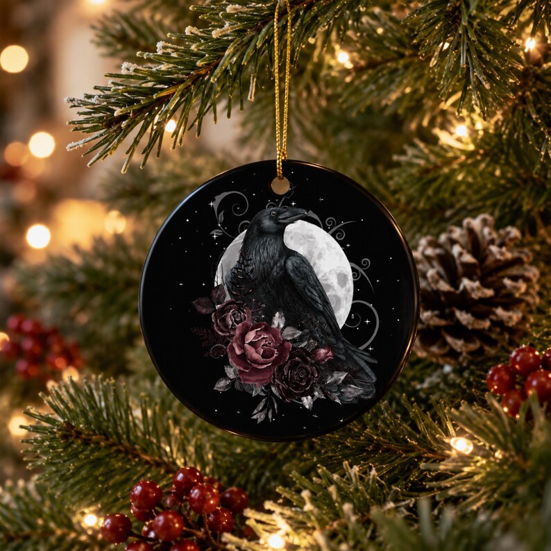 May include: A round black ceramic ornament featuring a detailed illustration of a black raven perched in front of a full moon, surrounded by dark red and deep purple roses with swirling vine accents, suspended by a thin gold metallic cord.
