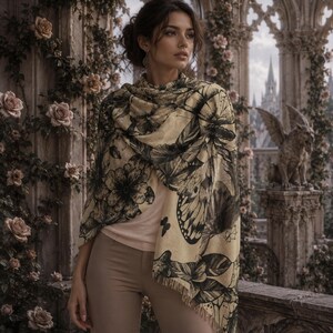 Peut inclure: Une &eacute;charpe beige orn&eacute;e d'un imprim&eacute; botanique et papillon noir avec un bord frang&eacute;, port&eacute;e sur un haut rose clair et un pantalon beige. L'&eacute;charpe pr&eacute;sente des illustrations d&eacute;taill&eacute;es de grandes fleurs, de feuilles et d'ailes de papillon.