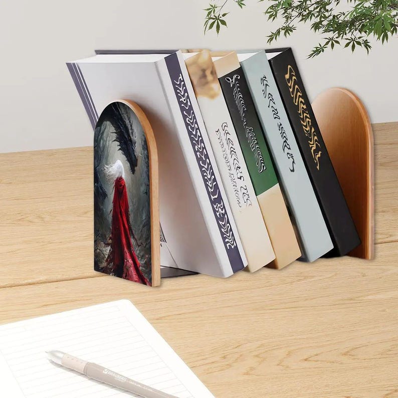 K&ouml;nnte beinhalten: Ein Paar gew&ouml;lbte Buchst&uuml;tzen aus Holz, die vier B&uuml;cher halten. Die linke Buchst&uuml;tze zeigt eine Illustration einer Figur in einem langen roten Umhang vor einem dunklen Drachen in einem Wald. Die rechte Buchst&uuml;tze besteht aus schlichtem, hellem Holz.