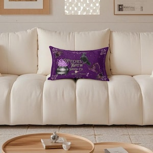 May include: A rectangular purple throw pillow featuring a graphic of a black cauldron filled with pink bubbles, a black crow, and a witch hat. The text reads Witches Brew Drink Co. and Always a Potion, surrounded by decorative floral corner accents.