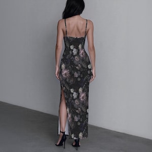 May include: A floor-length, sleeveless dress featuring a dark charcoal background with a muted floral print in shades of dusty pink, cream, and sage green. The garment has thin spaghetti straps, a fitted bodice, and a high side slit on the left leg.