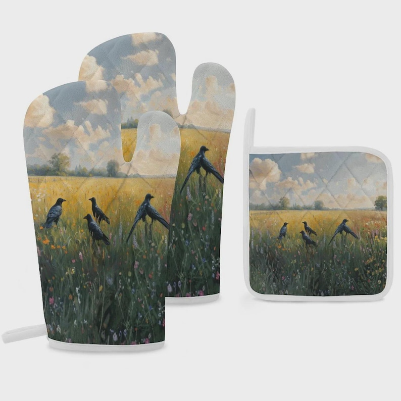 May include: A quilted oven mitt and a square pot holder featuring a printed landscape scene of black crows in a golden wheat field with wildflowers under a cloudy sky. Both items have white trim and a consistent painterly aesthetic design.