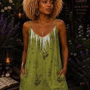 May include: A sleeveless olive green jumpsuit featuring a white drip pattern at the neckline, a dark botanical print, and the text "Always honor yourself all you give leads shoulder keep" printed in a script font on the lower front section.