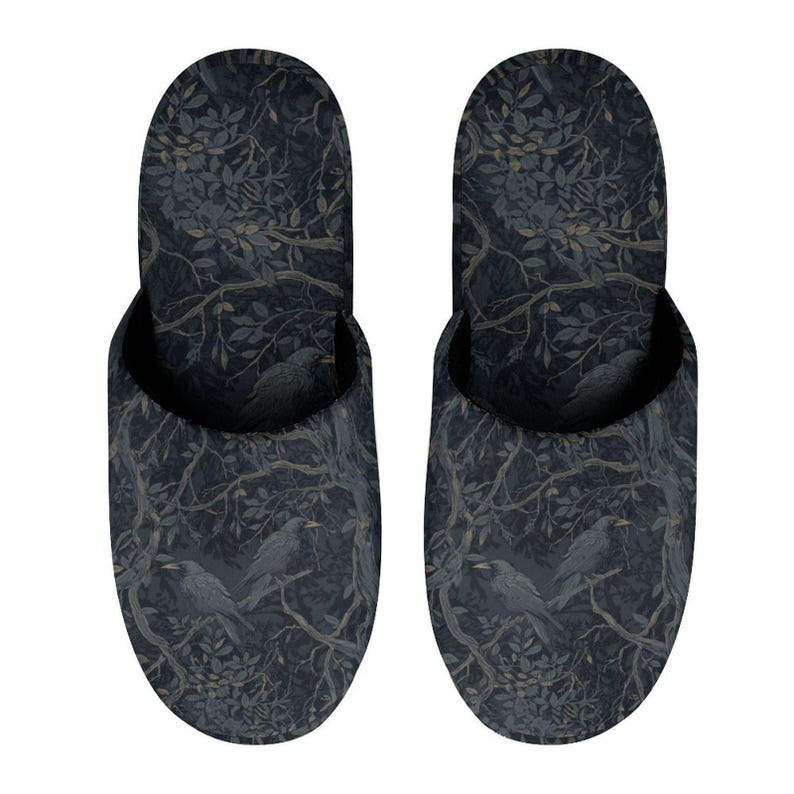 May include: A pair of slip-on slippers featuring a dark navy blue and charcoal gray pattern of crows perched on tree branches with dense foliage. The design covers the entire exterior of the footwear, showcasing a detailed botanical and avian motif.