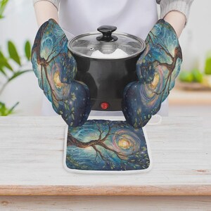 May include: A pair of oven mitts and a square pot holder featuring a dark blue and teal artistic print of a swirling tree under a night sky. The mitts are shown holding a black electric pot with a glass lid and a small red power indicator light.