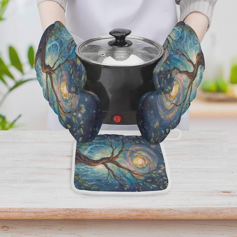 May include: A pair of oven mitts and a square pot holder featuring a dark blue and teal artistic print of a swirling tree under a night sky. The mitts are shown holding a black electric pot with a glass lid and a small red power indicator light.