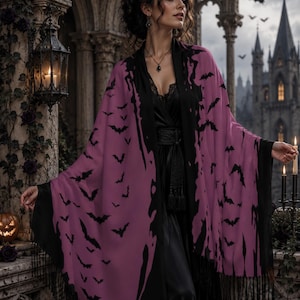 May include: A mauve shawl featuring a repeating black bat pattern and a black border with fringe. The garment is worn over a black dress with a lace neckline and a black waist belt. The shawl has a draped silhouette with long, flowing edges.