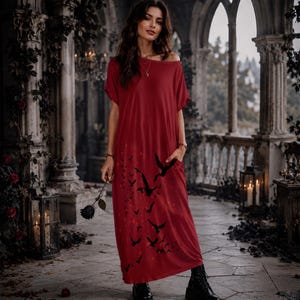 May include: A floor-length, short-sleeved red dress featuring a black bird silhouette print on the lower portion. The dress has a wide, off-the-shoulder neckline and side pockets. The fabric is solid red with a dark, graphic bird pattern.