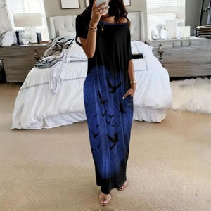May include: A floor-length short-sleeve dress featuring a black upper section that transitions into a blue lower section with a printed pattern of silhouettes of birds in flight. The garment includes side pockets and a wide, rounded neckline.