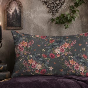 May include: A rectangular throw pillow featuring a dark gray background with a repeating pattern of black ravens, deep red roses, orange lilies, and small green leaves. The design includes tiny orange butterflies scattered among the floral elements.