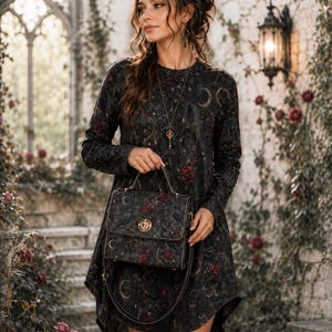 Könnte beinhalten: Ein langärmeliges schwarzes Kleid mit einem durchgehenden Muster aus roten Rosen, Mondsicheln und Raben. Das Kleid wird mit einer passenden strukturierten Handtasche kombiniert, die einen Tragegriff, einen Schulterriemen und einen runden goldenen Verschluss hat.