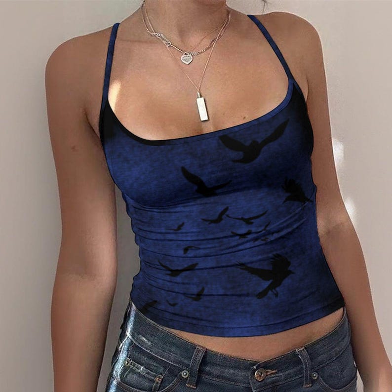 May include: A sleeveless tank top in a deep blue hue featuring a dark, mottled texture and a repeating pattern of black bird silhouettes in flight. The garment has a scoop neckline and thin shoulder straps, paired with blue denim jeans.