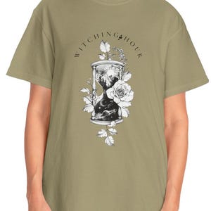 Può includere: Una t-shirt verde salvia con una grafica di una clessidra con un design floreale e il testo "Witching Hour".
