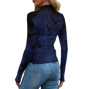 May include: A long-sleeve mock neck top featuring a dark blue and black gradient background with a repeating pattern of black bird silhouettes in flight. The garment has a fitted silhouette and is paired with light blue denim jeans.
