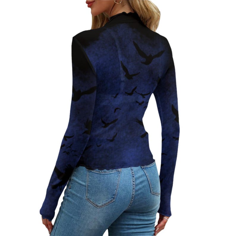 May include: A long-sleeve mock neck top featuring a dark blue and black gradient background with a repeating pattern of black bird silhouettes in flight. The garment has a fitted silhouette and is paired with light blue denim jeans.