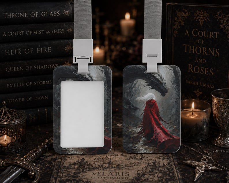 Puede incluir: Dos portatarjetas rectangulares con cordones grises. Uno tiene un inserto rectangular blanco, mientras que el otro muestra una ilustraci&oacute;n de fantas&iacute;a de una figura con una capa roja larga frente a un gran drag&oacute;n oscuro en un bosque.