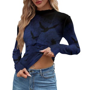 May include: A long-sleeve mock neck top featuring a dark blue and black gradient background with a repeating pattern of black bird silhouettes in flight. The garment has a fitted silhouette and a ruffled neckline edge, paired with blue denim jeans.