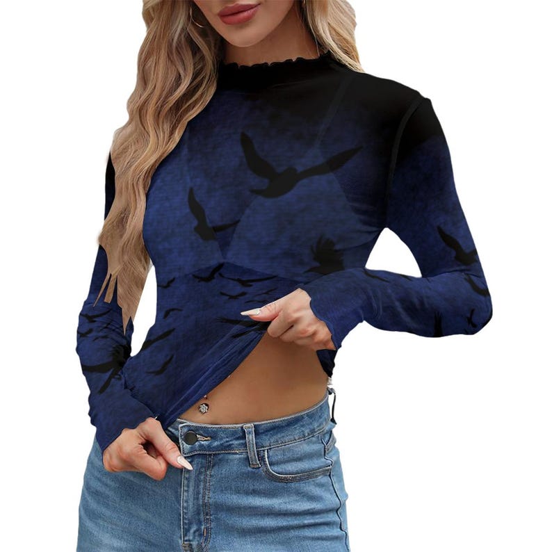 May include: A long-sleeve mock neck top featuring a dark blue and black gradient background with a repeating pattern of black bird silhouettes in flight. The garment has a fitted silhouette and a ruffled neckline edge, paired with blue denim jeans.