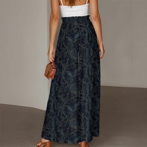 May include: A high-waisted maxi skirt in a dark navy blue hue featuring a repeating pattern of birds perched on intricate tree branches with leaves. The skirt has a gathered elastic waistband and a long, flowing silhouette that reaches the ankles.