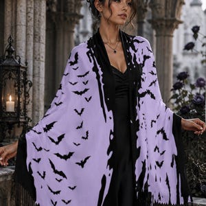 May include: A light purple shawl featuring a repeating black bat pattern and black fringe trim along the edges. The shawl is draped over a solid black garment, showcasing a contrasting color scheme with a distinct, jagged black border design.