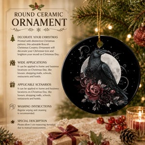 May include: A round ceramic ornament featuring a black raven perched beside dark red roses against a full moon background. The ornament is black with a gold hanging string. Text on the left side includes ROUND CERAMIC ORNAMENT and details.