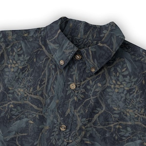May include: A button-down shirt featuring a dark navy blue background with a repeating pattern of tree branches, leaves, and birds in muted shades of gray, brown, and dark green. The shirt has a pointed collar and light brown circular buttons.